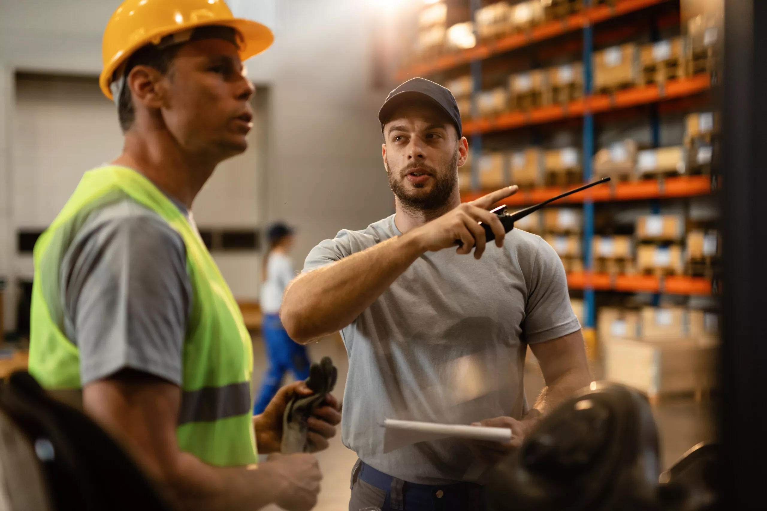 Warehouse dispatcher talking with a worker in industrial storage compartment.